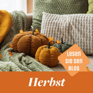 Gemütliche Herbstdekoration mit Stoffkürbissen in Orangerot und Grün, weichen Kissen, einer Tagesdecke und Lichterkette. Mit der Aufschrift „Herbst“ und einem orangen Button „Lesen Sie den Blog“.